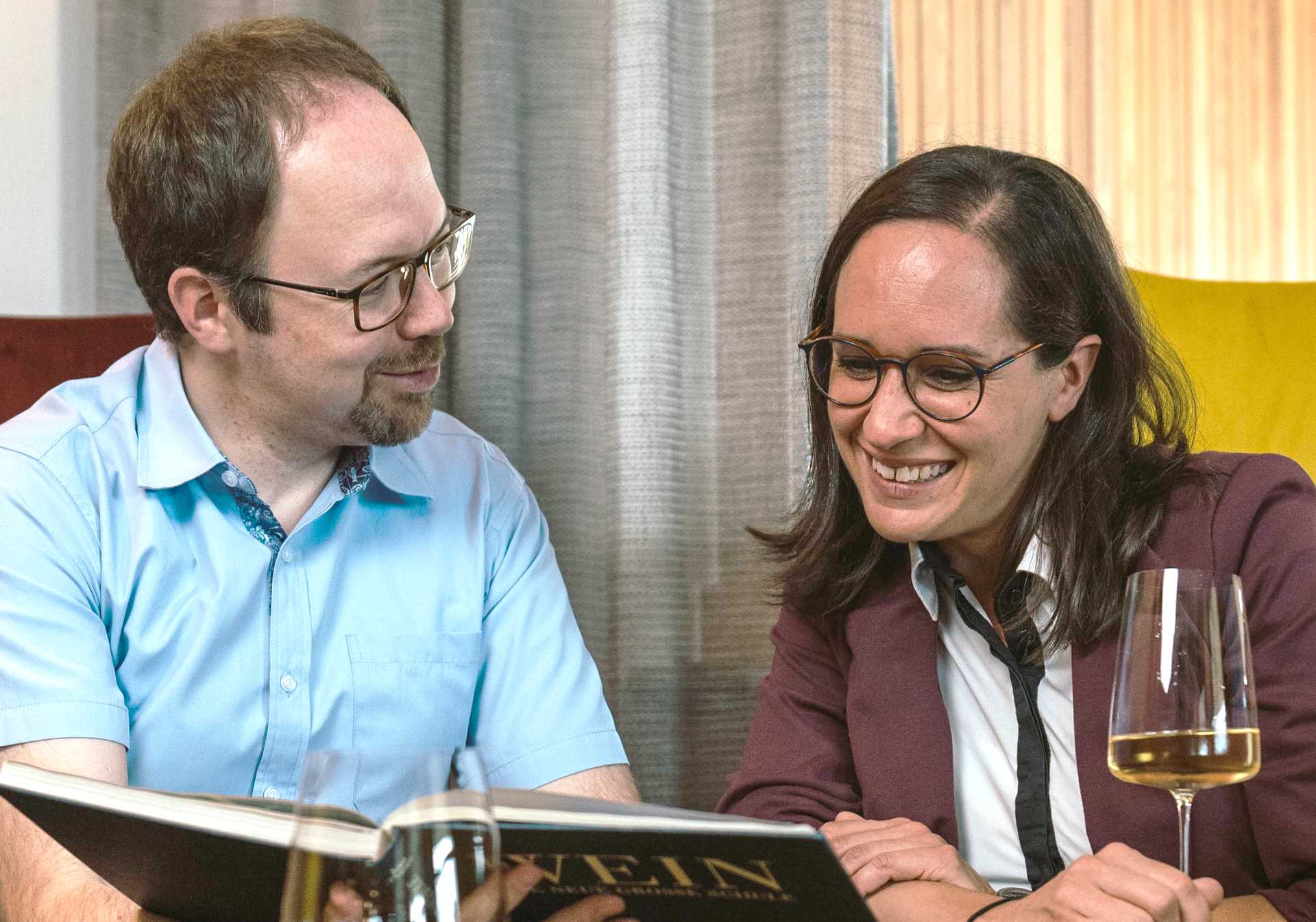 Christa und Heiner Christof mit einem Glas Wein und einem Buch über Weine