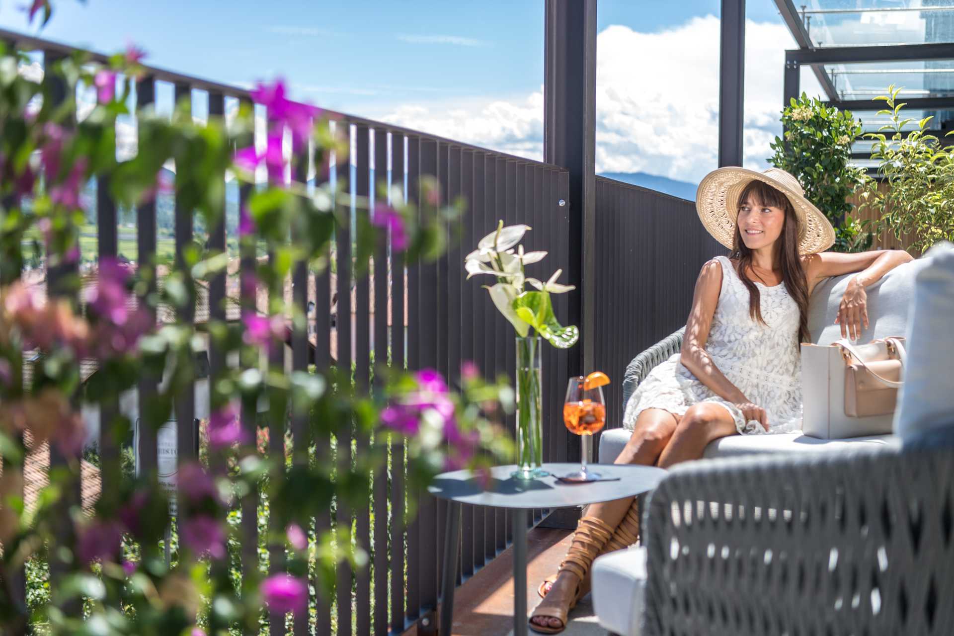 Woman sits in the lounge outdoor area and enjoys the sun with a drink.
